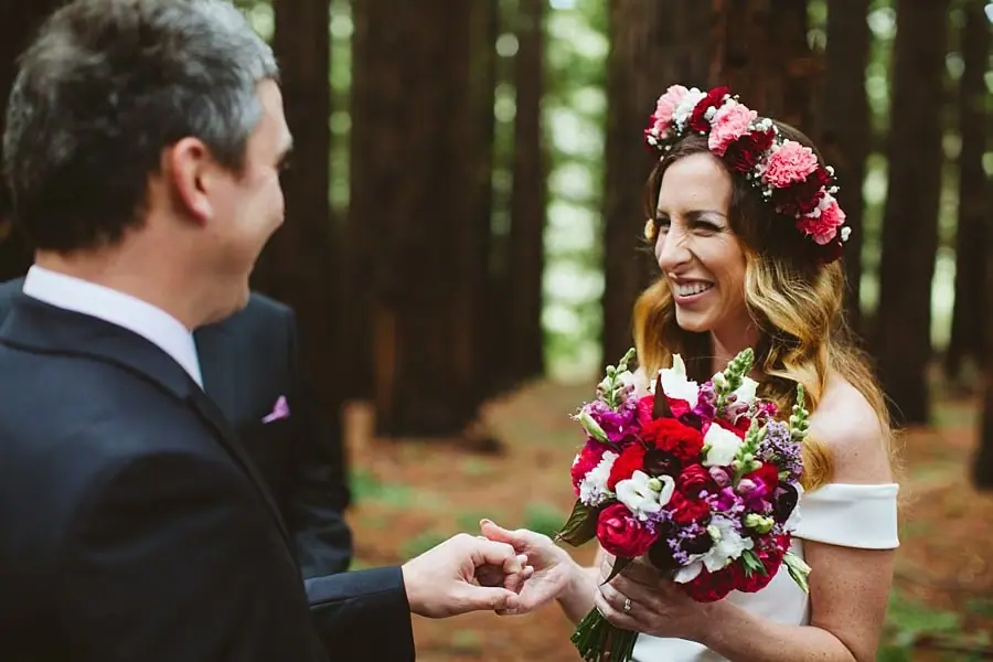 Bride smiling at the groom as he holds her hand during their forest ceremony.