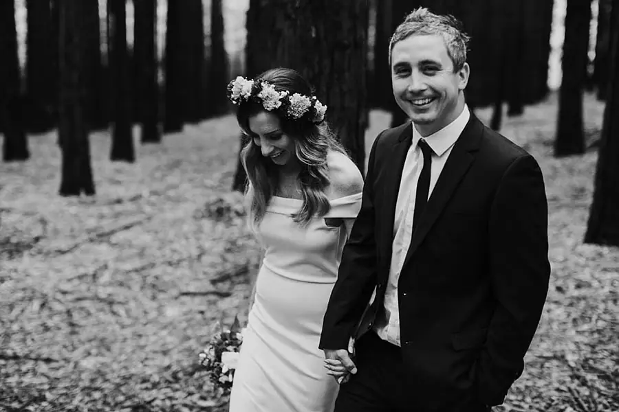 Black-and-white photograph of newlyweds walking together through the redwood forest.