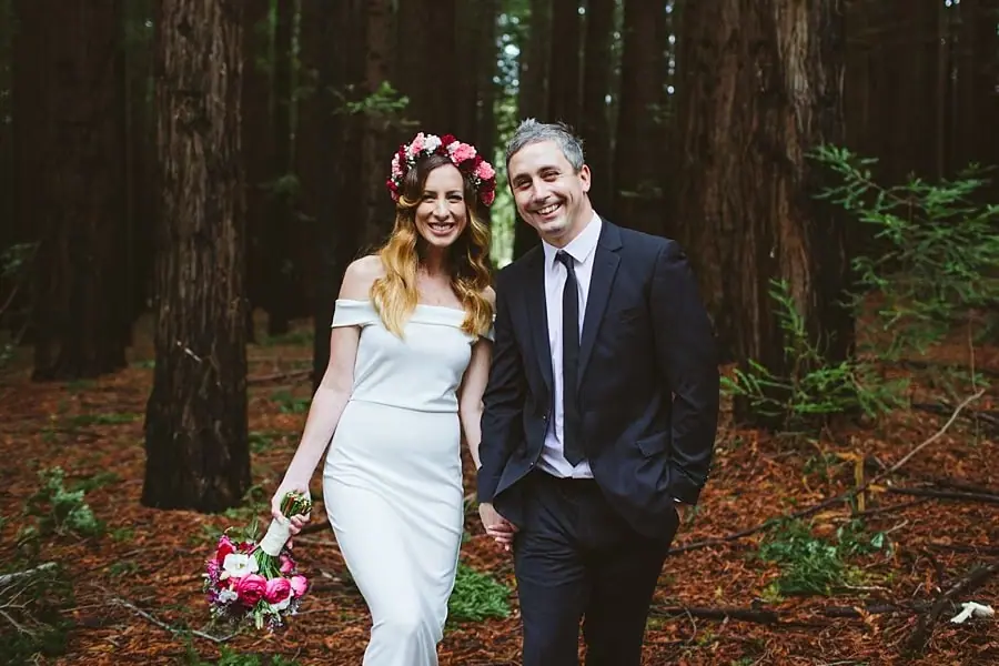 Bride and groom smiling side by side beneath the redwood trees.