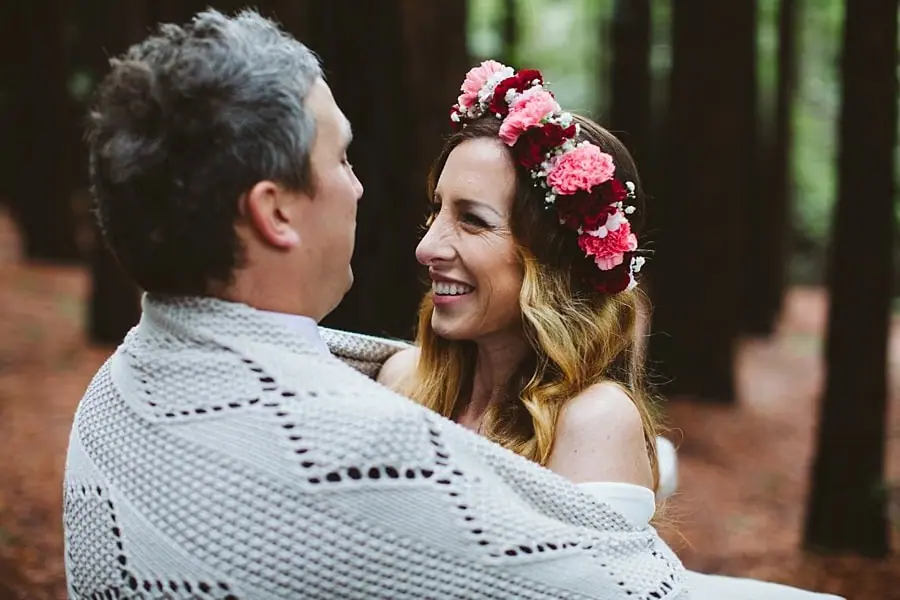 Bride smiling at the groom while both are wrapped together in a grey knit blanket.