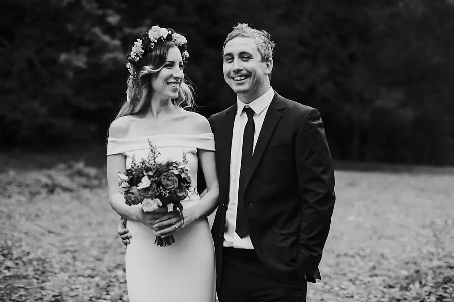 Black-and-white portrait of newlyweds smiling side by side, the bride holding her bouquet.