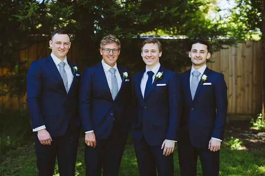 Four men in navy suits posing together in a garden.
