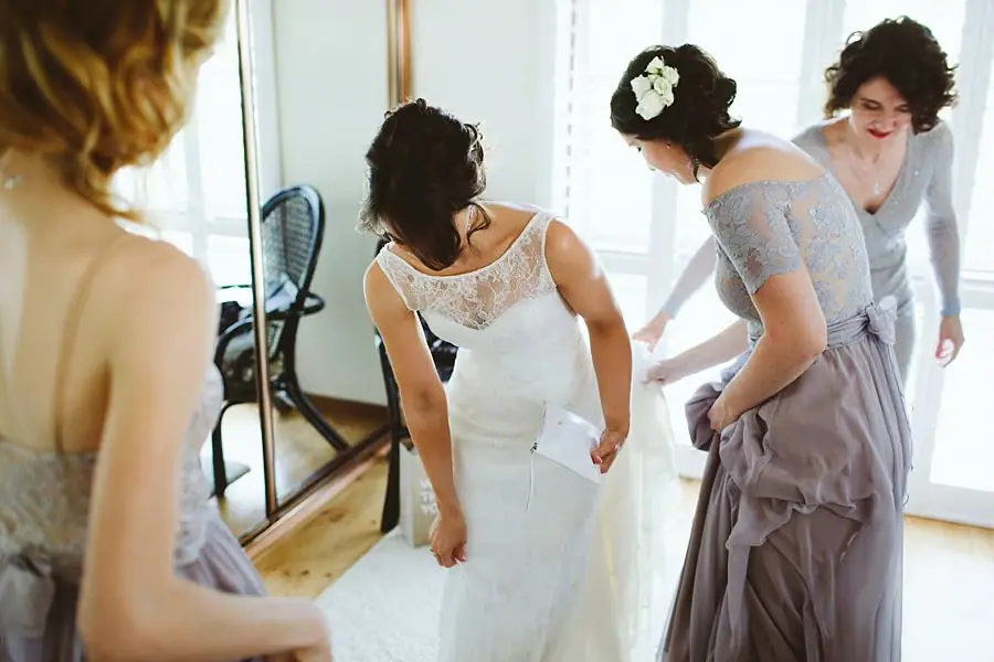 Bride looking down at her dress while women stand beside her.