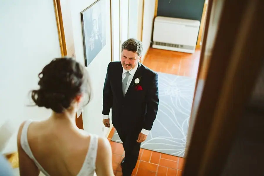 Suited man smiling up at the bride from the foot of a staircase.