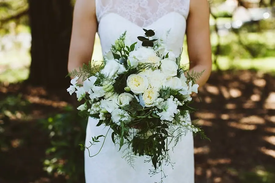 Close-up of the bride holding a bouquet of white flowers and greenery.