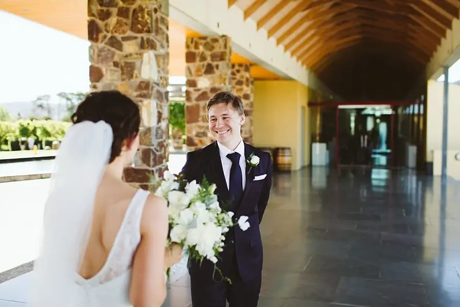 Groom smiling at the bride beneath a timber roof beside stone pillars.