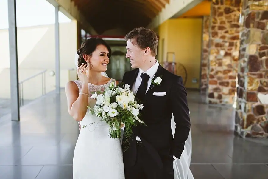 Bride and groom smiling at each other beneath the covered walkway.