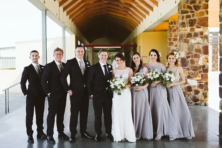 Wedding party posing between stone pillars beneath a timber roof.