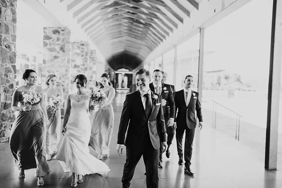 Black-and-white photograph of the wedding party walking along a covered walkway.