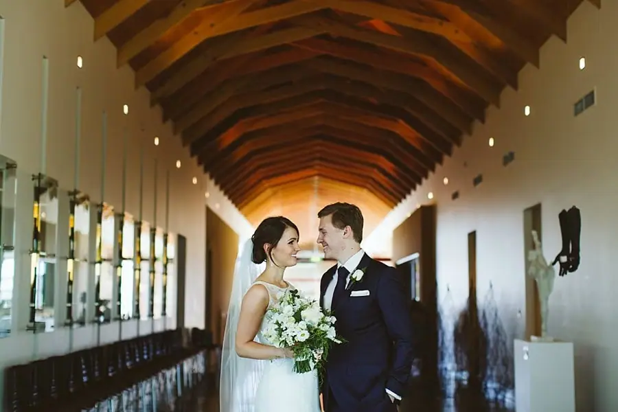 Couple standing together beneath a long timber-roofed walkway.