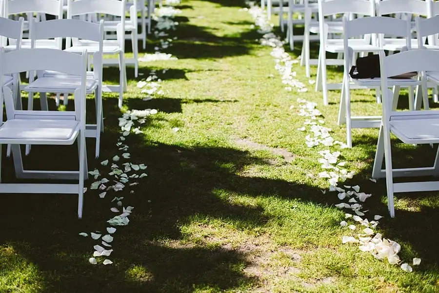 White flower petals lining a grassy ceremony aisle between rows of white chairs.