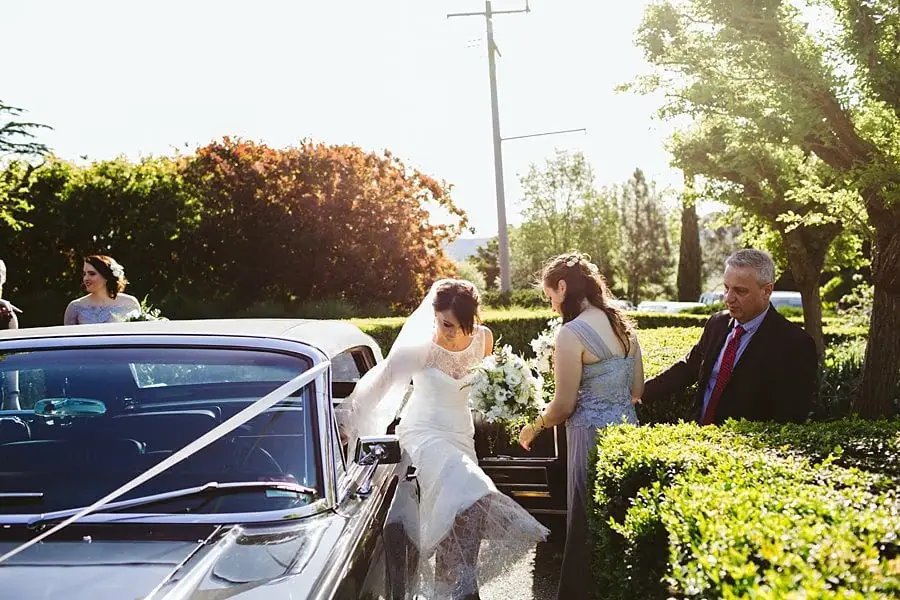 Bride stepping out of a convertible beside waiting wedding guests.