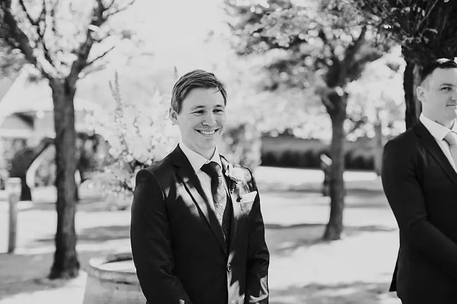 Black-and-white portrait of the groom smiling beneath trees.