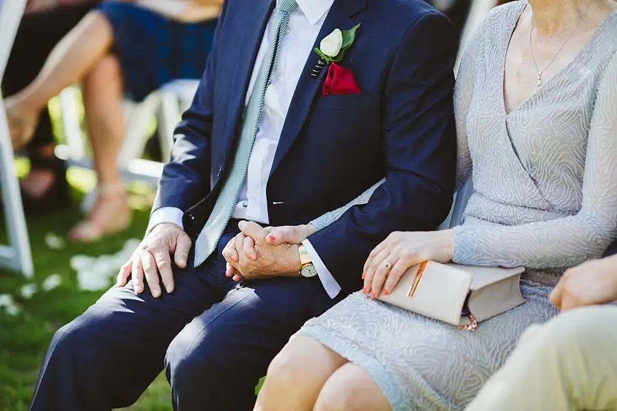 Close-up of seated guests holding hands during the wedding ceremony.
