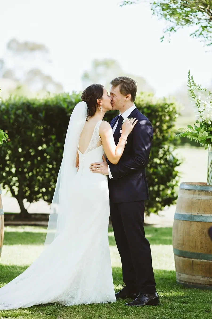 Bride and groom kissing beside a flower-topped wine barrel.