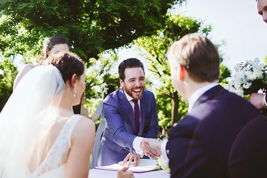 Smiling guest shaking the groom's hand beside the signing table.