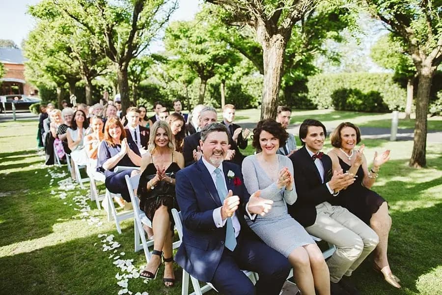 Wedding guests smiling and applauding from rows of white chairs.