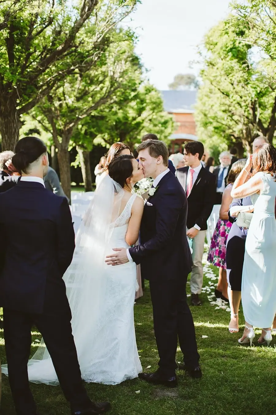 Bride and groom kissing among guests after the outdoor ceremony.