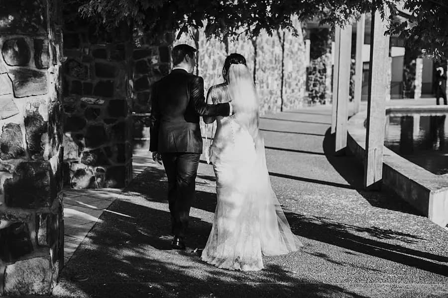 Black-and-white photograph of the couple walking beside a stone wall and open doorway.