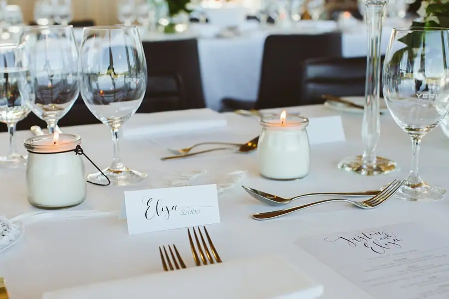 Reception place setting with candles, wine glasses, cutlery and a handwritten name card.