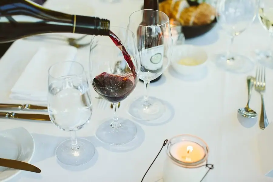 Red wine being poured into a glass beside a candlelit place setting.