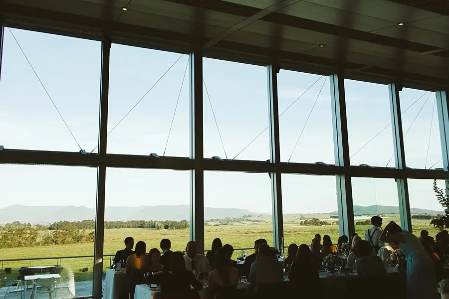 Guests silhouetted against reception windows overlooking fields and hills.