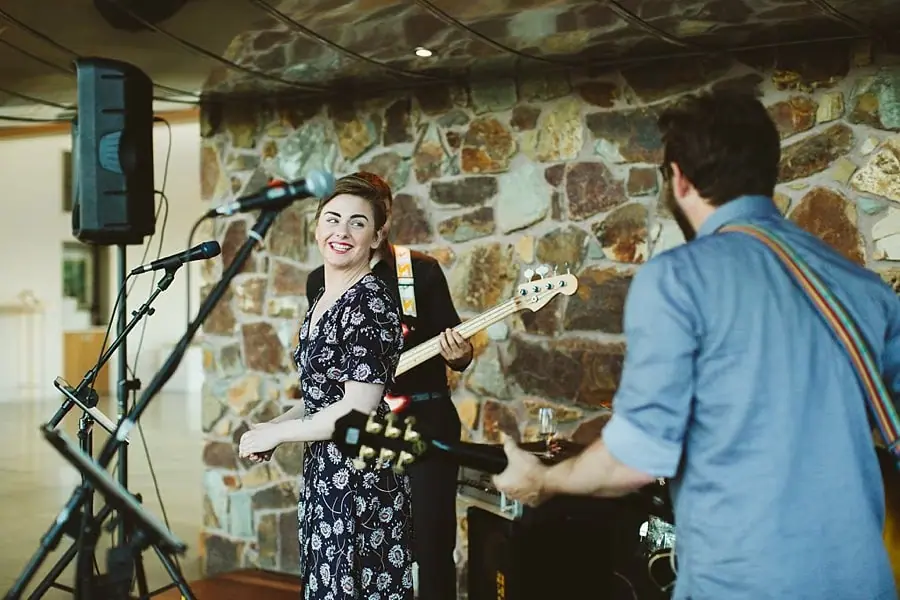 Two musicians with guitars performing beside a stone wall.