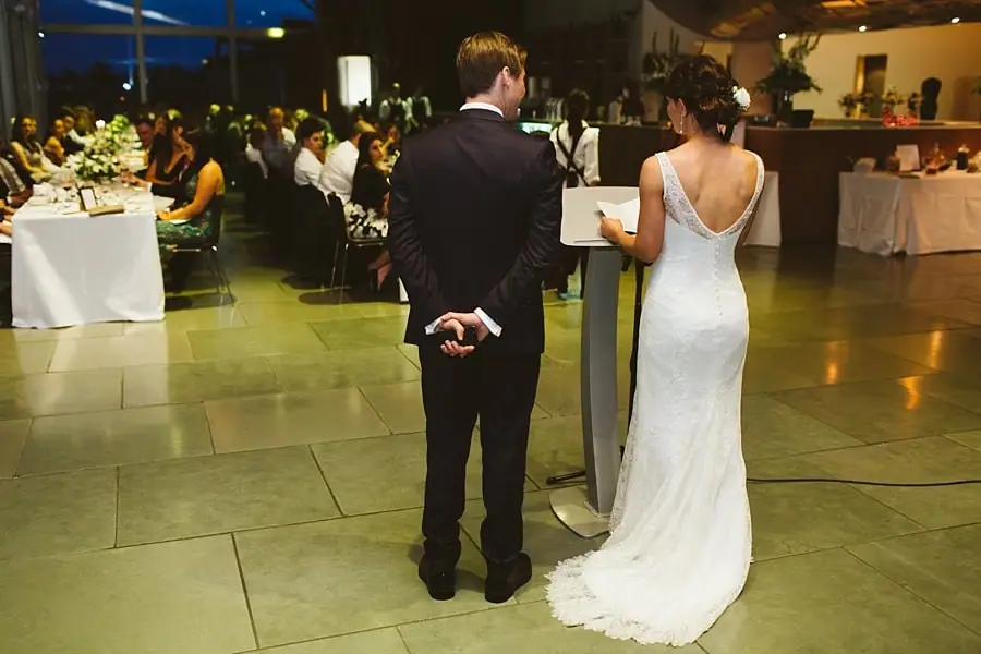 Bride speaking into a microphone beside the groom in the reception room.