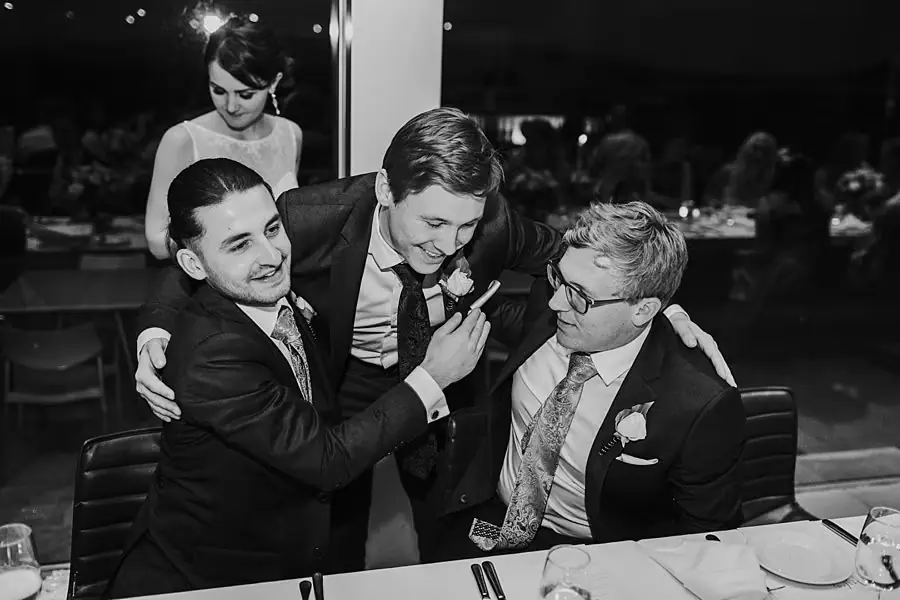 Black-and-white photograph of men laughing together around a reception table.