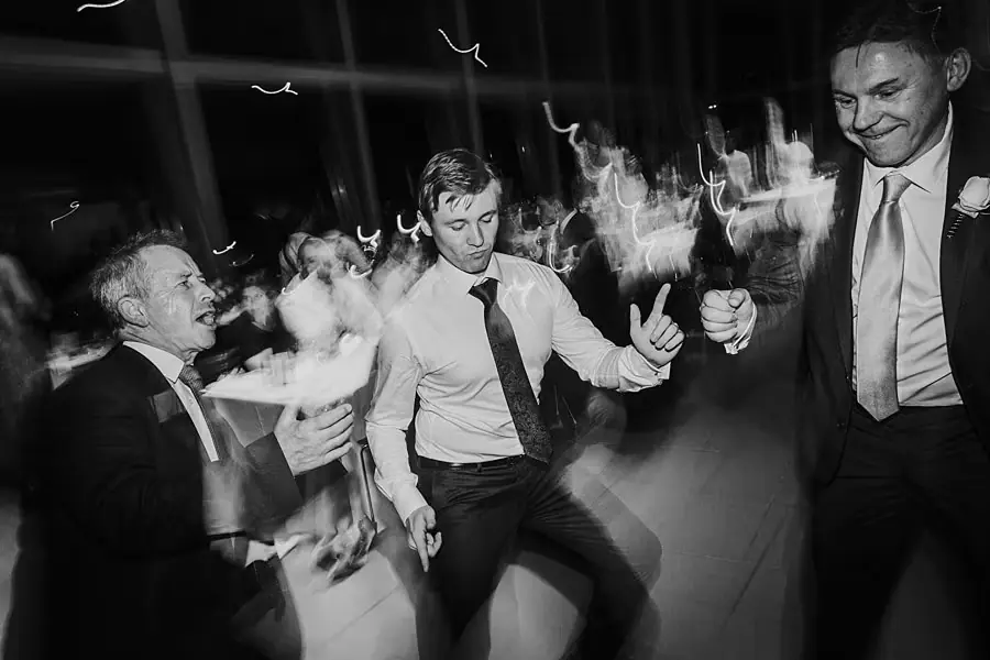 Black-and-white photograph of suited men dancing together at the reception.