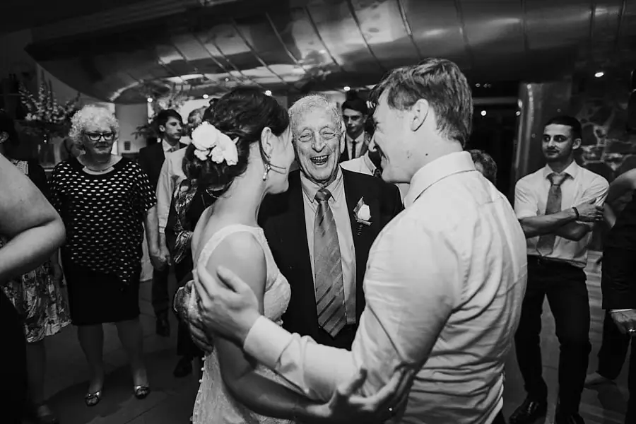 Black-and-white photograph of the bride and groom dancing among smiling guests.