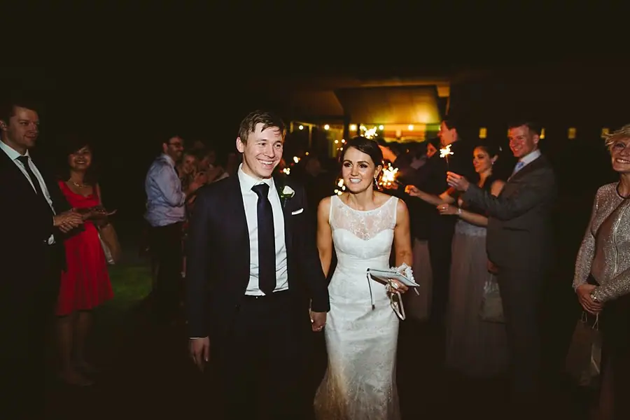 Bride and groom smiling as they walk between guests at the reception.