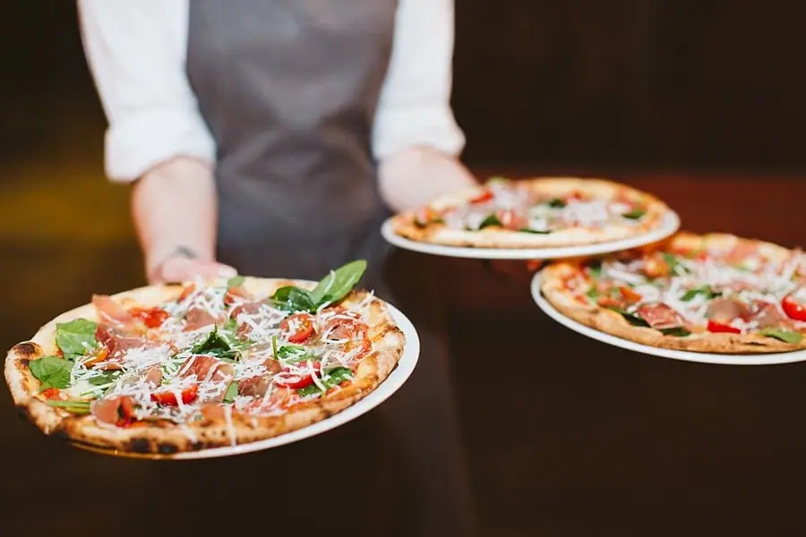 Server carrying three pizzas on white plates.