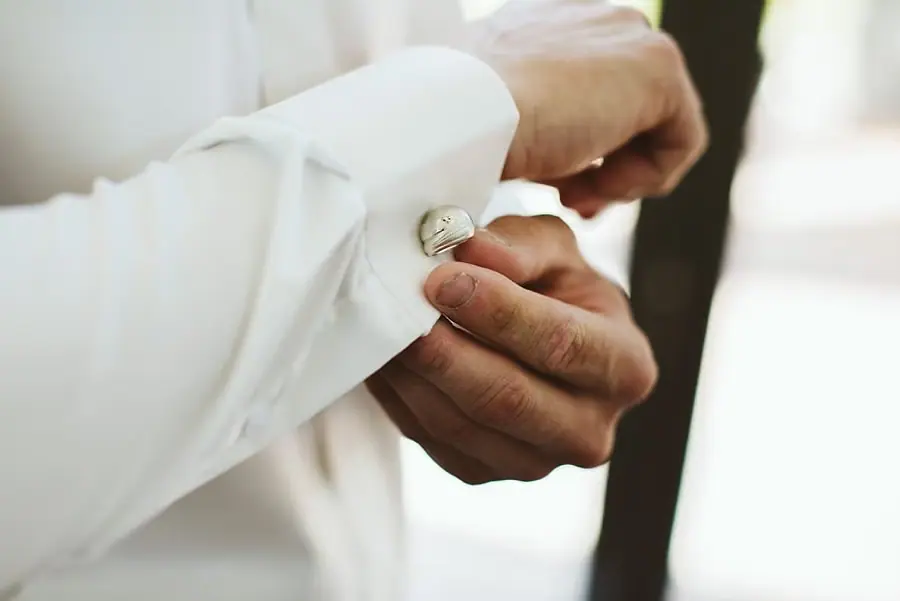 Close-up of a man fastening a cufflink on his white shirt sleeve.
