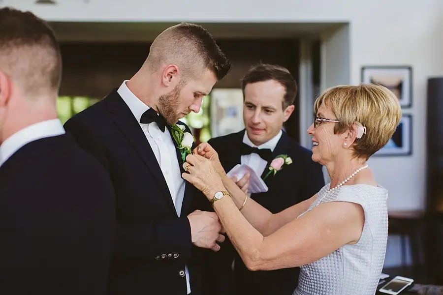 Woman pinning a flower buttonhole onto a man's dark suit jacket.