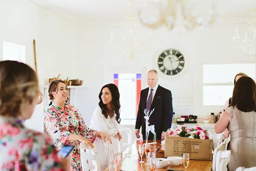 Bride and companions chatting around a kitchen island during preparations.
