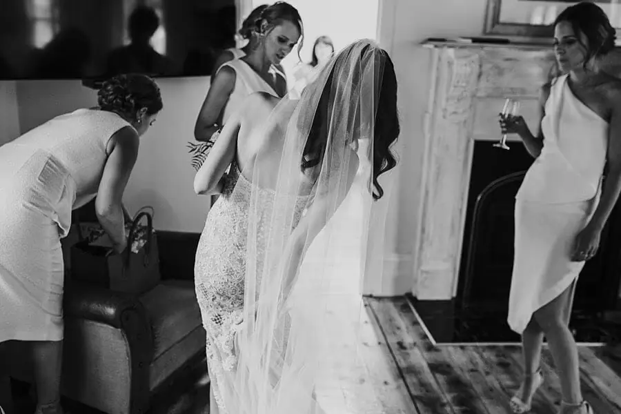Black-and-white photograph of women arranging the bride's veil in a bedroom.