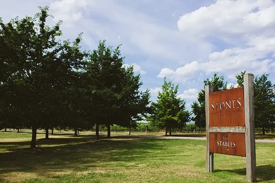 Rust-coloured venue sign beside a lawn and rows of leafy trees.
