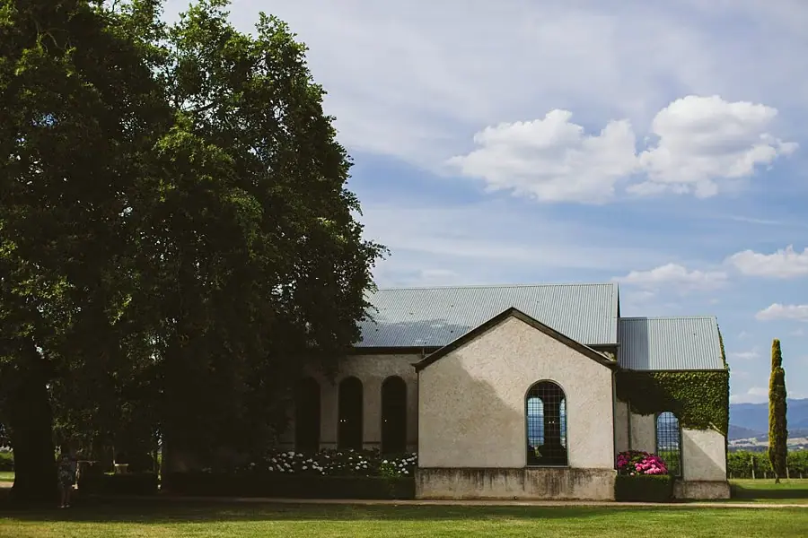 Stone chapel with arched windows on a green lawn beneath a cloudy sky.