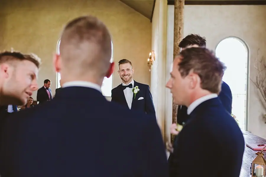 Groom smiling at companions gathered inside the chapel.