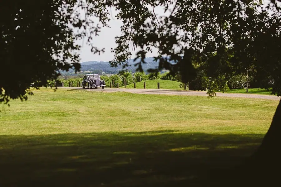 Vintage car crossing a lawn toward the chapel beyond leafy branches.