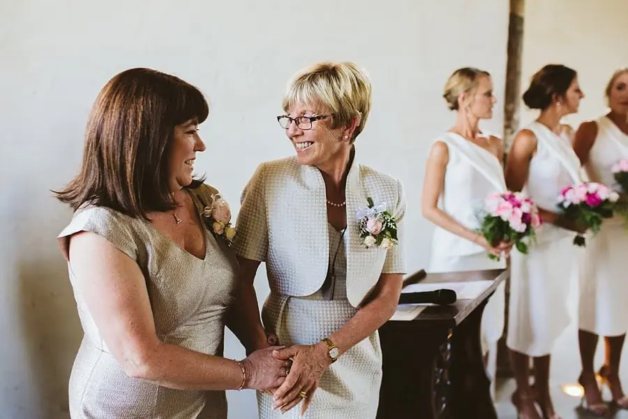 Two women holding hands and smiling beside the bridesmaids during the ceremony.