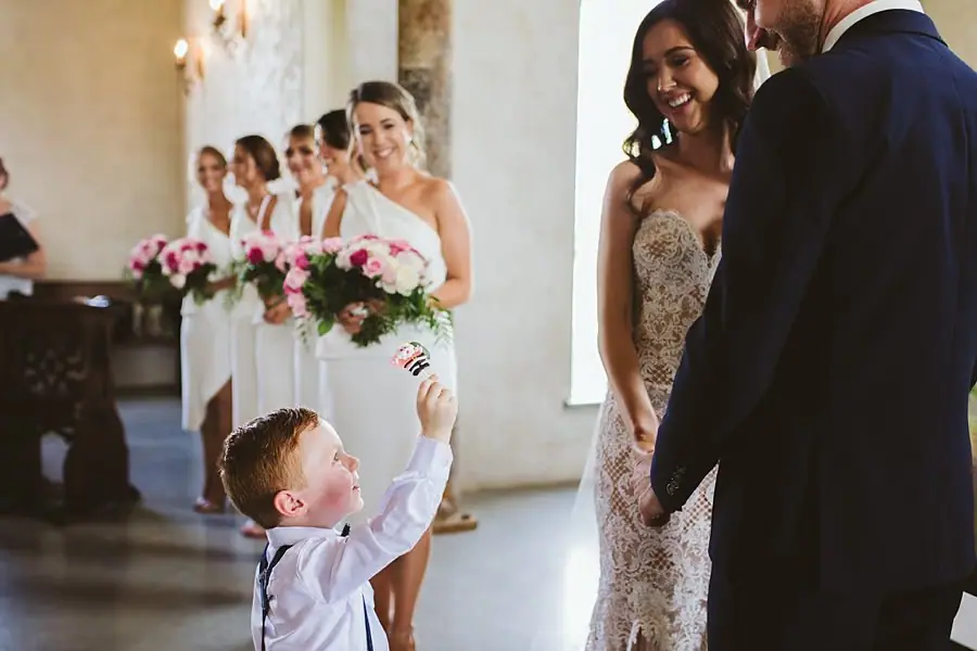 Small boy reaching up toward the bride as the groom stands beside her.