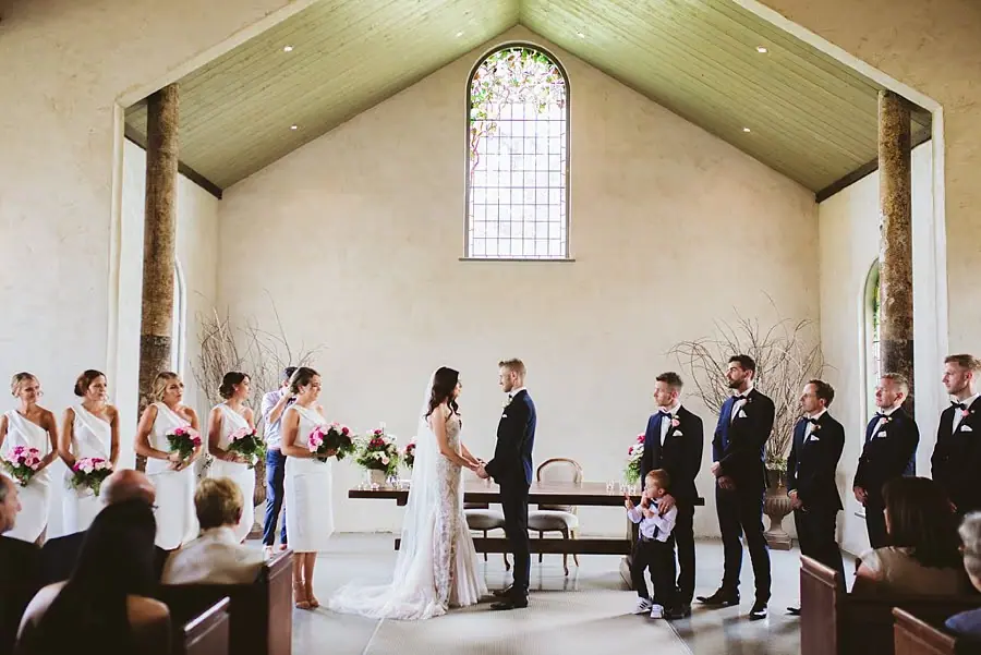 Wide view of the wedding party beneath the chapel's tall stained-glass window.