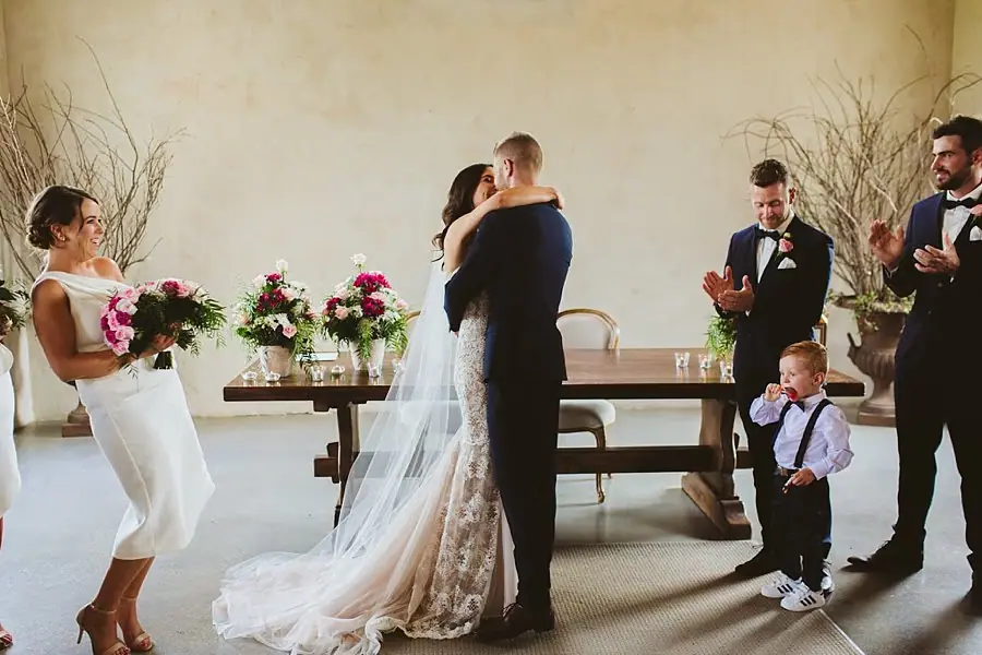 Bride and groom kissing while their wedding party applauds inside the chapel.