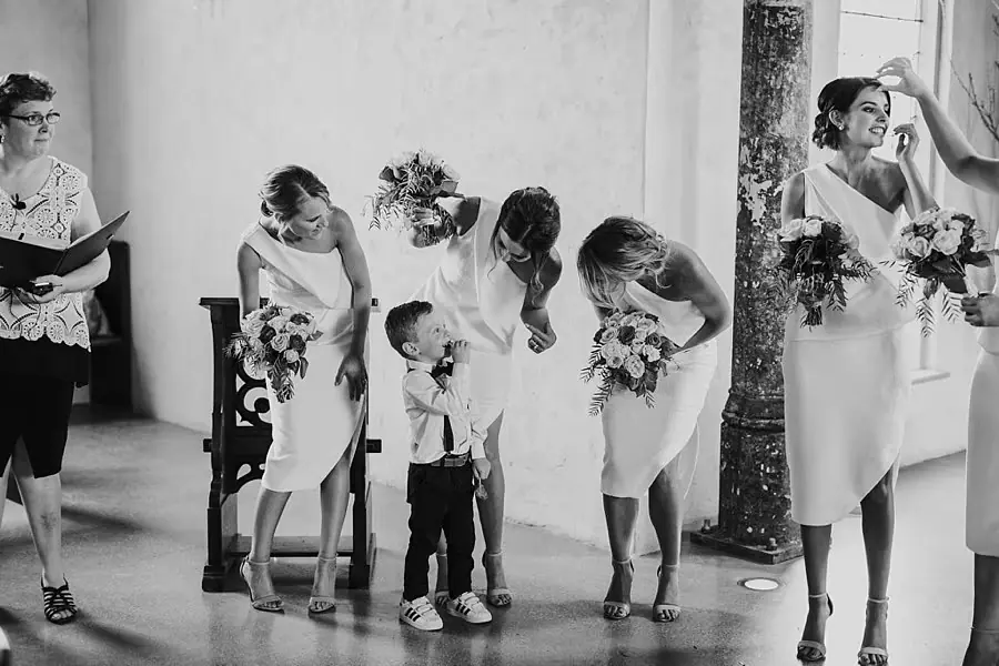 Black-and-white photograph of bridesmaids smiling and bending toward a small boy.