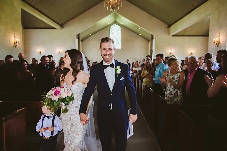 Bride and groom walking down the chapel aisle with a small boy beside them.