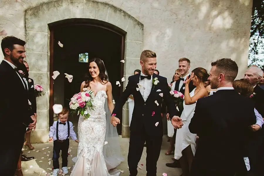 Bride and groom leaving the chapel as guests throw pale flower petals.