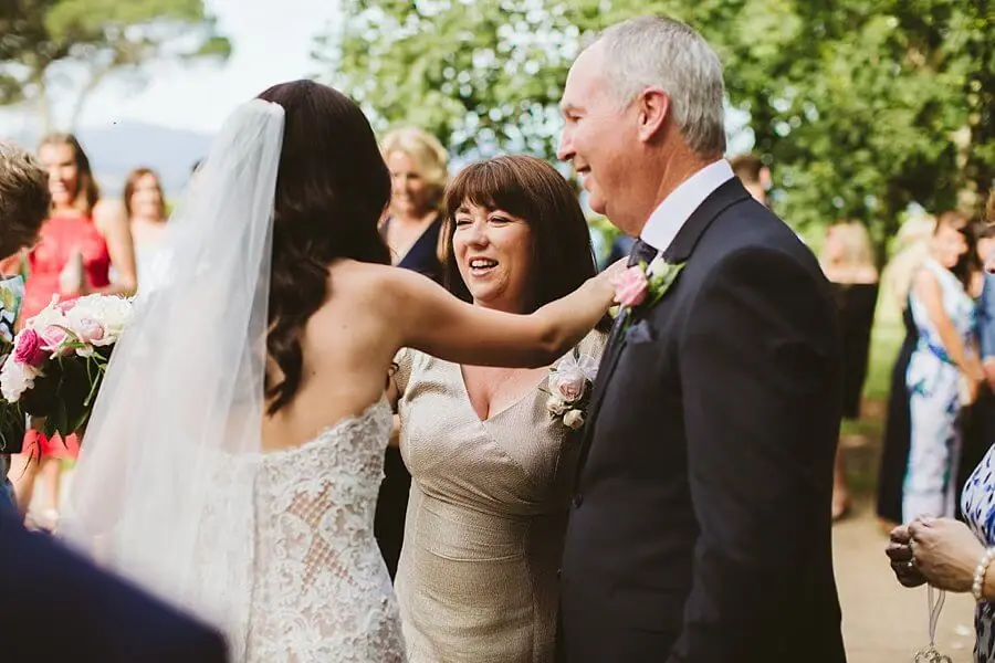 Bride greeting a woman and man among gathered guests outside the chapel.