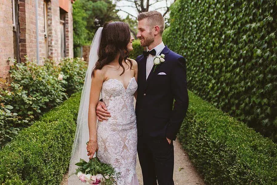 Couple embracing on a narrow garden path between brick walls and ivy.